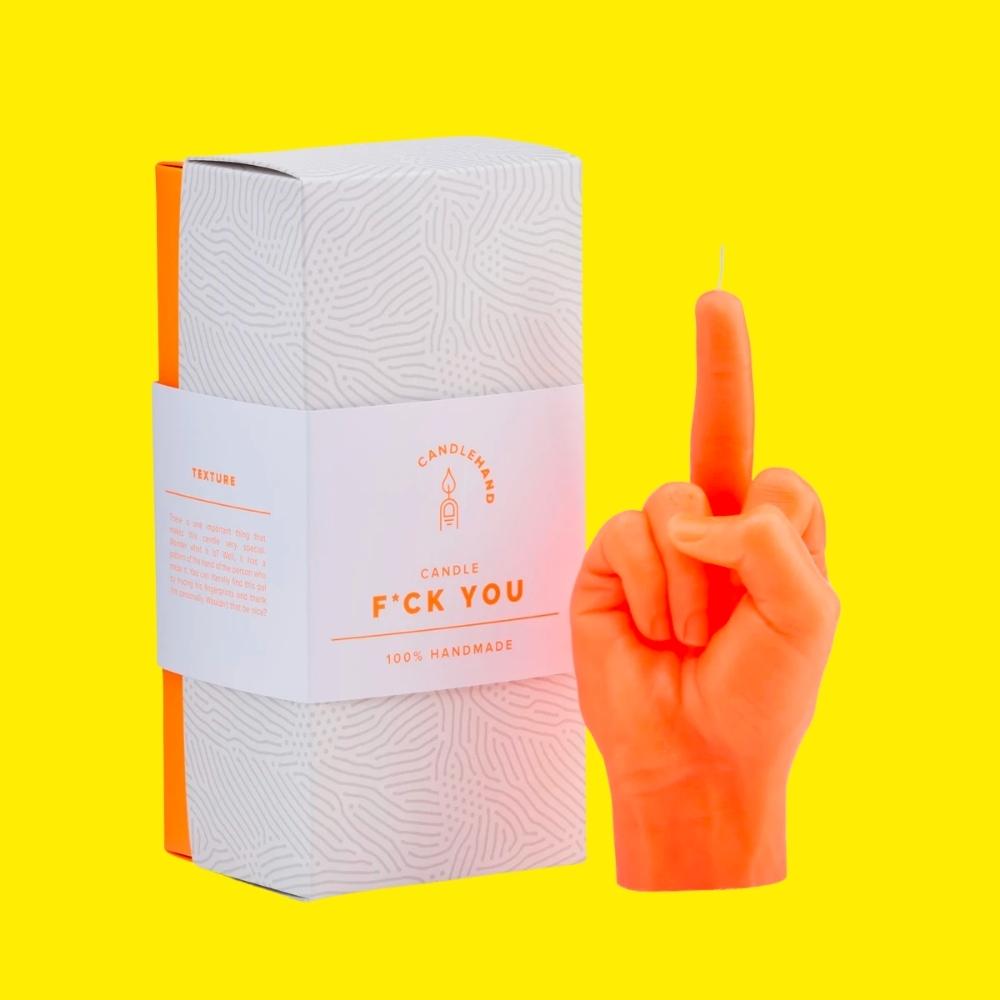 Sweary humanlike hand gesture orange wax candle with gift box on a yellow background