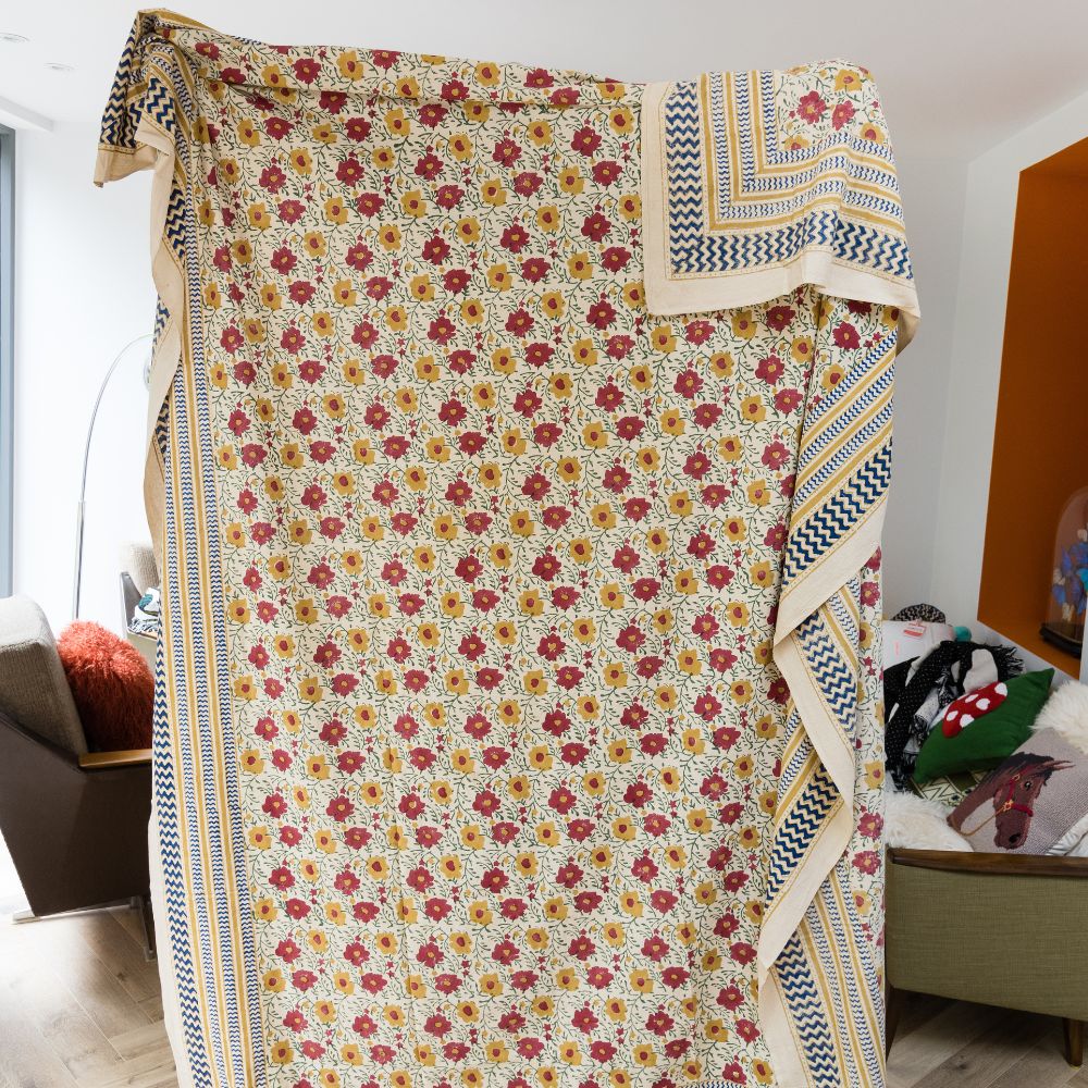 Living room setting with person holding up a vintage style hand printed floral throw blanket with yellow and red flowers on