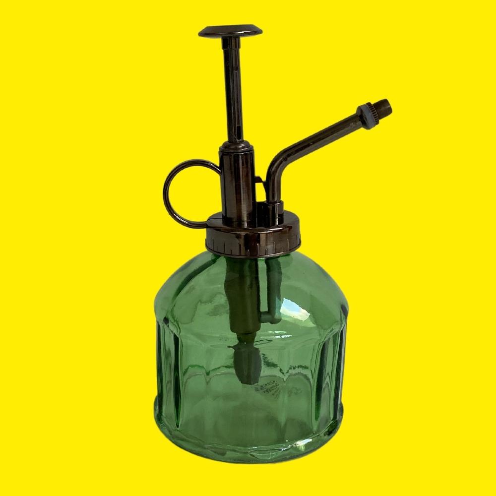 Green glass plant spray bottle mister on a yellow background