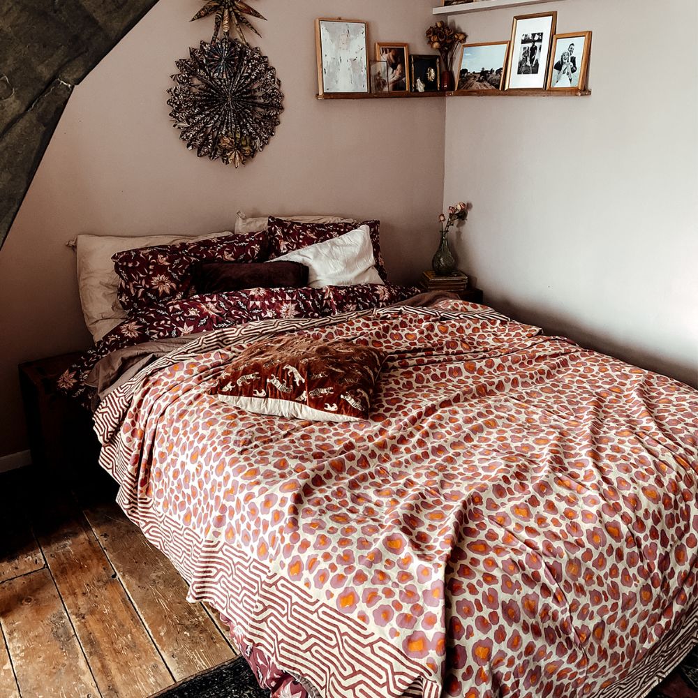 Bedroom scene with pink, red and orange cotton handprinted leopard throw blanket by Doing Goods