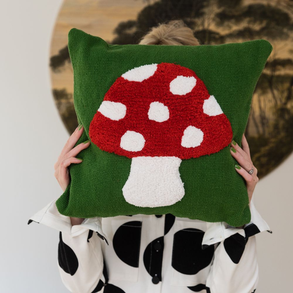 Person holding a green cushion with a red spotted toadstool mushroom cottagecore style tufted motif on