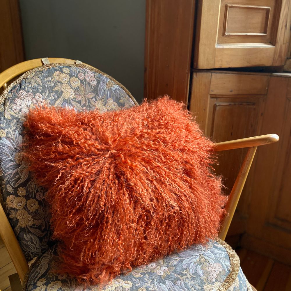 Burnt orange shaggy Mongolian sheepskin fur cushion on a rocking chair