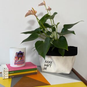 canvas plant pot cover with plant that says please don't die on a table with a candle and some books