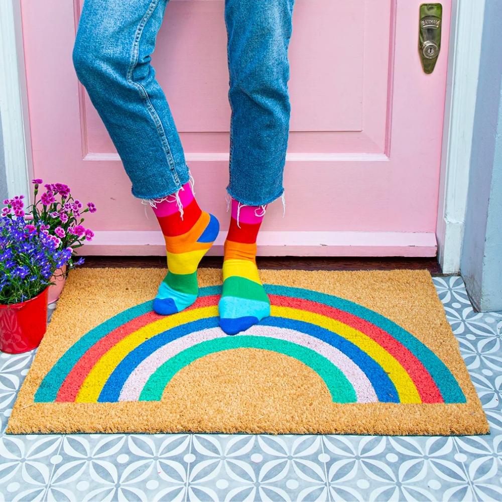 Pink front door with person wearing rainbow socks stood on a sustainable multicoloured rainbow doormat porch decor ideas