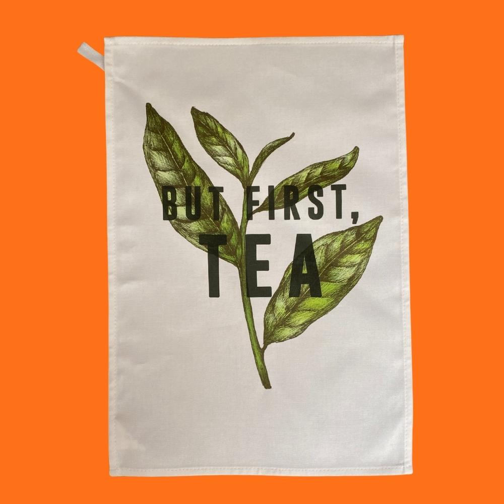 white cotton tea towel with large green tea leaves and the words but first tea in black