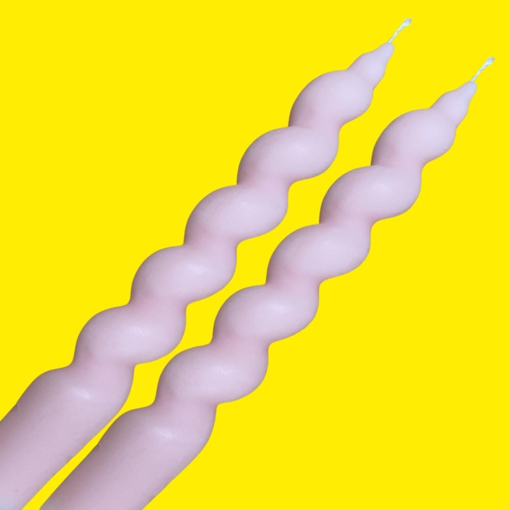two pink twisted tapered dinner soy wax candles on a yellow background