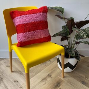 shaggy pink and red large stripe cushion on a yellow chair with plant next to it