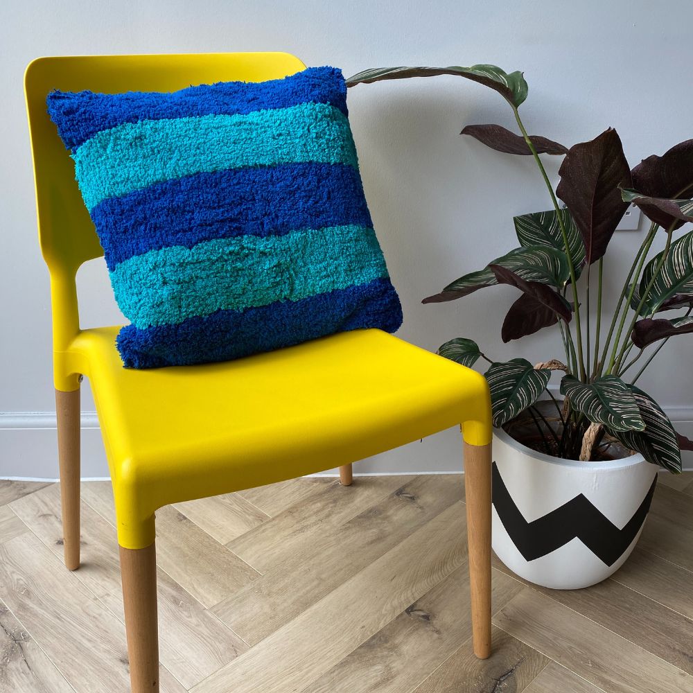 shaggy textured blue stripe cushion on a yellow chair with next to black and white plant pot