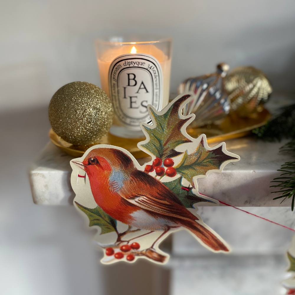 fireplace mantle piece with candle, baubles and a sustainable paper christmas garland with robin bird motifs