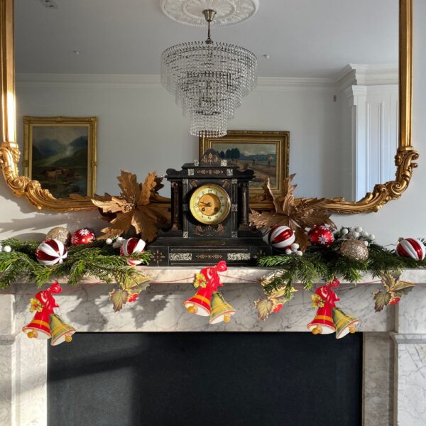 fireplace with mirror and clock with a festive vintage style sustainable paper christmas decoration wreath garland bunting with holly leaves and bells in red and green