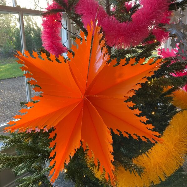 oversized orange recycled plastic star on a Christmas tree with orange and yellow eco-friendly tinsel