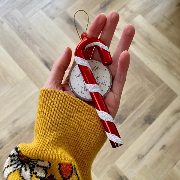 a hand holding a red and white stripey striped candy cane Christmas decoration